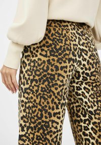 Los pantalones de mezclilla con estampado de leopardo presentan un patrón marrón y negro con un acabado texturizado, detalles en los bolsillos traseros y un diseño de cintura alta.