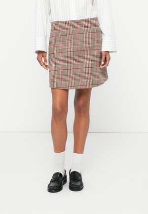 Jupe mini à carreaux dans des tons beige, rouge et marron avec un tissu texturé. Associée à des chaussettes blanches montantes et des mocassins noirs.