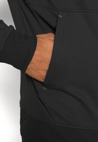 Sweatshirt noir avec une poche avant, à la texture douce et aux poignets côtelés, conçu pour le confort et la fonctionnalité.