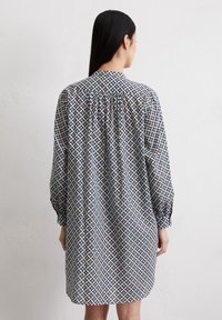 Langärmliges Kleid mit einem blau-weißen geometrischen Muster und gelben Akzenten, aus leichtem Stoff und mit einem Raffdetail im Rücken.