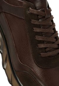 Zapatillas de cuero marrón con material texturizado, costuras en contraste y cordones oscuros; suela de goma redondeada con un agarre estampado.