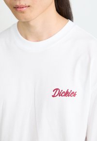 White cotton t-shirt featuring a red embroidered "Dickies" logo on the left chest. Round neckline and standard fit.