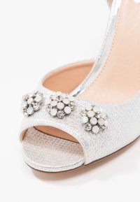 Escarpin argenté à bout ouvert avec trois grappes d'embellissements en strass blancs et transparents sur la bride avant.