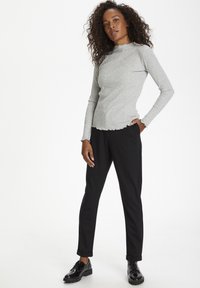 Grå ribbet langærmet bluse med bølget kant, parret med sorte slim-fit bukser og glansfulde sorte snørebåndssko.