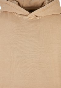 Beige színű pamut kapucnis pulóver, elől kenguruzsebbekkel, húzható kapucnival és puha tapintással. Minimalista dizájn, amelyben egy diszkrét márkajelzés található belül.