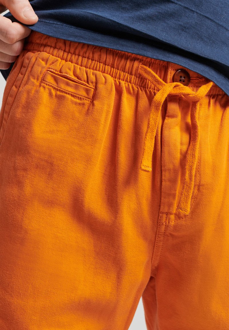 Pomarańczowe bawełniane szorty z elastycznym paskiem, z małą kieszonką i detalem w postaci guzika. Miękka tekstura i luźny krój.