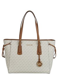Sac fourre-tout beige Michael Kors avec des poignées en cuir tan, motif logo MK et breloque ronde logo MK suspendue à l'avant.