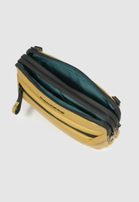 Gelb-schwarze Tasche mit Reißverschluss und glatter, matter Textur. Innenausstattung mit türkisfarbenem Futter und Organisationsfächern.