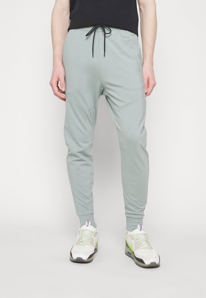 Jogging léger gris clair avec une taille élastique et un cordon de serrage noir. Possède des jambes fuselées et des détails de panneau latéral. Le porteur les a associés à des baskets.