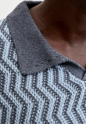 Close-up of dark skin neck wearing a knitted sweater with a grey textured collar and zigzag pattern in light and dark grey.
