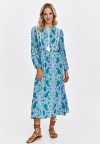 Sukienka maxi w niebiesko-zielony wzór paisley, z długimi rękawami i marszczonym pasem. Posiada wiązanie przy szyi i frędzle dekoracyjne.