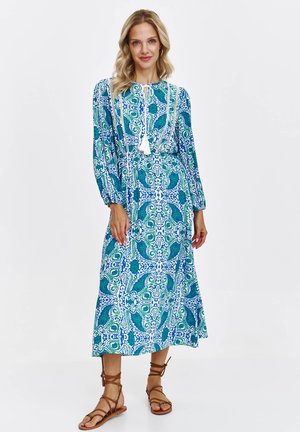 Sukienka maxi w niebiesko-zielony wzór paisley, z długimi rękawami i marszczonym pasem. Posiada wiązanie przy szyi i frędzle dekoracyjne.