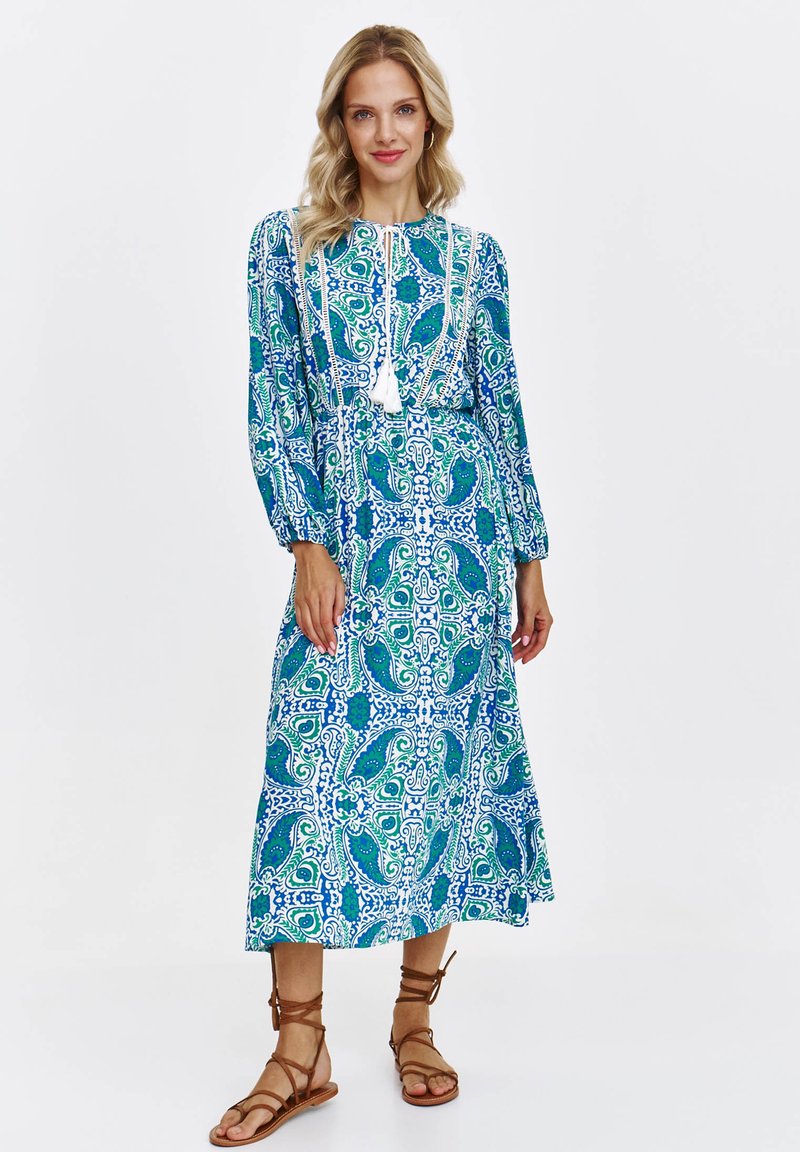 Sukienka maxi w niebiesko-zielony wzór paisley, z długimi rękawami i marszczonym pasem. Posiada wiązanie przy szyi i frędzle dekoracyjne.