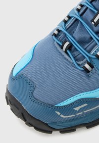 Blauer Sportschuh mit strukturiertem Mesh-Obermaterial, verstärkter Zehenkappe, kontrastierenden hellblauen Akzenten und schwarzer Gummisohle mit Profil.