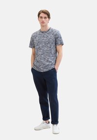 Short-sleeve, crew-neck T-shirt with a textured blue and white pattern, paired with navy trousers and white sneakers.