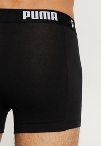 Mustad mustad bokserid pehmest kangast, millel on lai must vöö, millel on valge "PUMA" logo, siledat tekstuuri ja õmblustega detailid.