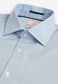 Chemise à rayures bleu clair avec un col boutonné et trois boutons sur le devant. Étiquettes visibles à l'intérieur du col. Texture de tissu douce.