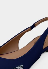 Πλατφόρμα υποδήματος γιατί με λουράκι σε ναυτικό μπλε χρώμα, με καφέ εσωτερική επένδυση και χαμηλό τακούνι, με μερικό λευκό λογότυπο στο εξωτερικό μέρος.