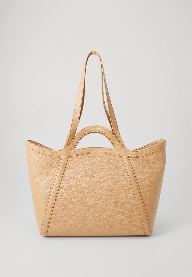 Tan leather tote bag with a textured finish, curved handles, and a spacious design. Features exposed stitching and structured sides.
