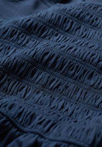 Navy blue fabric with gathered texture; features alternating rows of elastic shirring, creating a rippled effect across the surface.