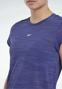 Fialové sportovní tričko s texturovaným pruhovaným vzorem, kulatým výstřihem a krátkými rukávy. Obsahuje malé bílé logo na prsou.