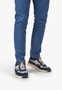 Marinblå och grå träningsskor i mesh och mocka, krämfärgad sula och beige detaljer. Bärs med blå tajta byxor.