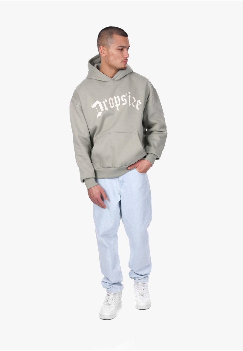 Sweat à capuche gris clair avec poche avant et texte "Dropslee". Associé à un pantalon bleu clair et des baskets blanches, créant un look décontracté et relax.