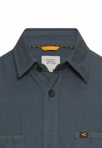 Donkergrijs overhemd met knoopsluiting, voorzien van een klassieke kraag, twee borstzakken, gele binnenlabel en contrasterende stikdetails.