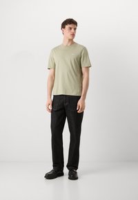 Lys grøn kortærmet t-shirt med et lille logo, parret med mørke denim bukser og sorte sko. Simpelt design, afslappet pasform.