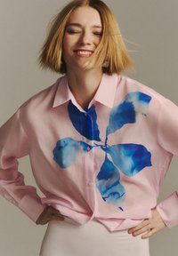 Camicia button-up rosa con una grande stampa floreale astratta blu sulla parte anteriore. Maniche lunghe e colletto classico. Tessuto liscio.