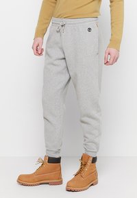 Grijze sweatpants met elastische tailleband en trekkoord, zijzakken en een klein logo.detail. Gepaard met tan werklaarzen met veters.