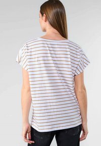 Camiseta blanca con rayas beige horizontales, mangas cortas tipo capucha y un corte relajado. La tela parece suave con un detalle mínimo.