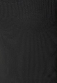 In primo piano, texture di tessuto nero a coste che mostra linee verticali e sfumature sottili.