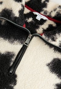 Zwart-wit gespikkelde fleece pullover met een hoge kraag, voorzien van een zwarte rits en een rode binnenvoering. Etiket leest "NEXT."