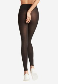 Zwarte leggings gemaakt van glad, rekbaar materiaal met een elastische tailleband; gedragen met witte sneakers; aansluitend design.