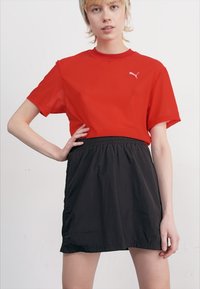 Röd kortärmad t-shirt med rund halsringning och vitt logotyp, ihop med en svart minikjol med elastisk midja gjord av lätt material.