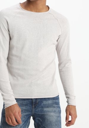 Lysegrå langærmet skjorte lavet af blødt strikstof. Har rund halsudskæring og raglanærmer. Kombineret med blå denimjeans.