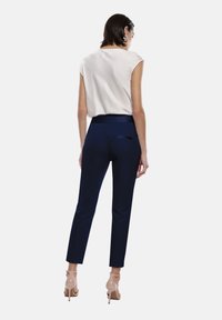 Pantaloni da cerimonia blu con una texture liscia e una vestibilità slim. Presentano una cintura in satin e una piccola tasca sul retro. Abbinati a un top leggero senza maniche.