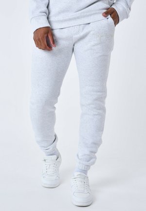 Pantalons de survêtement gris clair en tissu doux, avec une taille élastique et des poignets élastiques, ornés d'un logo brodé discret sur la cuisse gauche.