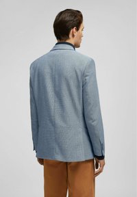 Lichtblauwe blazer van een gestructureerde stof, met gestructureerde schouders en een reverskraag. Heeft schuine zijopeningen en een slanke pasvorm.