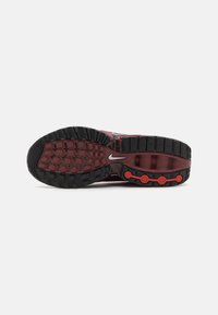 Nike sportinių batų padas, kuriame matomos juodos guminės dalys su raudonomis detalėmis, tekstūruotas raštas ir apvalūs amortizaciniai elementai.