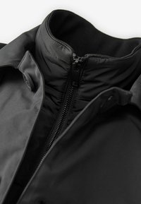 Schwarze isolierte Jacke mit hohem Kragen, einem durchgehenden Reißverschluss und glatter Stofftextur mit minimaler Gestaltung.