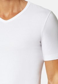 T-shirt blanc à col en V à manches courtes, fabriqué en tissu coton lisse. Présente un design ajusté et des lignes épurées sans logos ni motifs visibles.