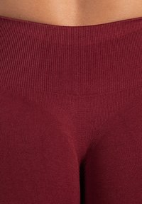 Bordowe legginsy z ribbowanym wysokim pasem i gładką teksturą. Charakteryzują się dopasowanym krojem i subtelnym odcieniem. Brak widocznych wzorów.