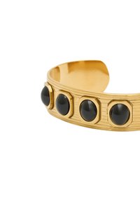 Złota bransoleta mankietowa z fakturowaną powierzchnią, z pięcioma wyraźnymi czarnymi kamieniami szlachetnymi osadzonymi w sześciokątnych akcentach wzdłuż opaski.