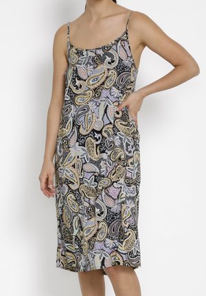 Femme portant une robe midi sans manches à fines bretelles avec un motif cachemire multicolore, posant avec une main sur la hanche.