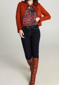 Giacca in suede color ruggine, blusa floreale con fiocco, jeans in denim scuro e stivali di pelle marroni al ginocchio. Dettaglio con zip sulla giacca.