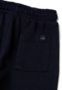 Tmavě modré tepláky s elastickým pasem, bočními kapsami a zadní kapsou s malou štítkovou logem. Měkká, texturovaná látka.