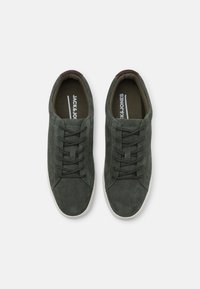 Gröna mockaskor med vita gummisulor, med en klassisk snördesign och texturerade detaljer på ovandelen.