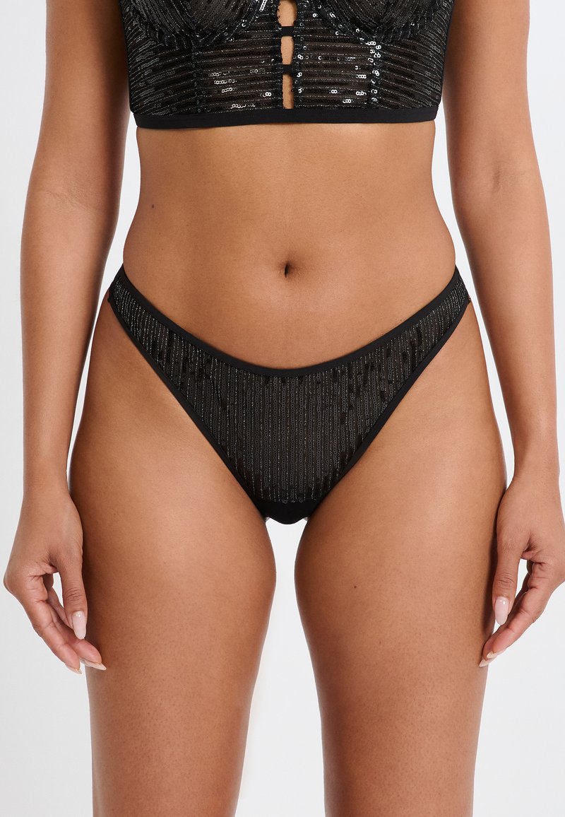 Slip bikini neri con design a coste arricchito da paillettes per una texture particolare, caratterizzati da un taglio a vita bassa e sottili cinturini laterali.